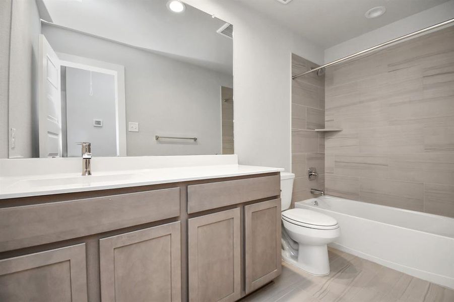 Indulge in refined charm in the secondary bathroom, where the tile flooring harmonizes with a bath/shower combo surrounded by tasteful tile. Slate wood cabinets, coupled with a gorgeous countertop, elevate the space, cultivating a truly welcoming atmosphere. Sample photo, as built color and selections will vary.