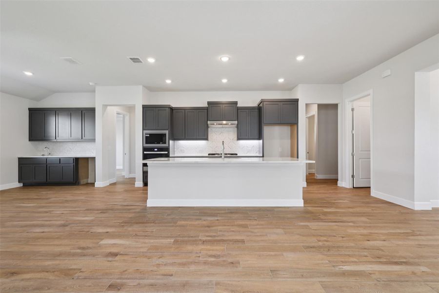 Kitchen featuring backsplash, a center island with sink, light wood-style floors, light countertops, and recessed lighting