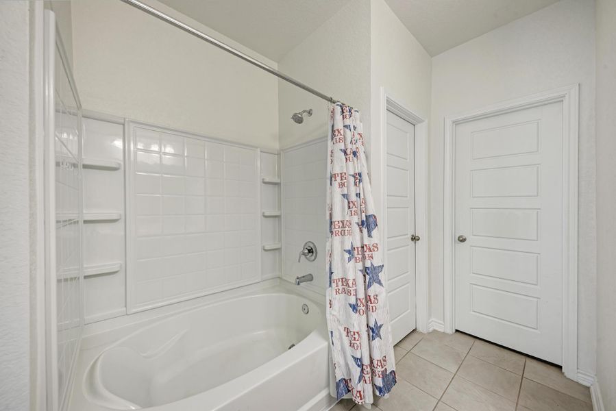 A well-maintained bathroom with a tub and shower combination, featuring tile flooring and clean white doors.