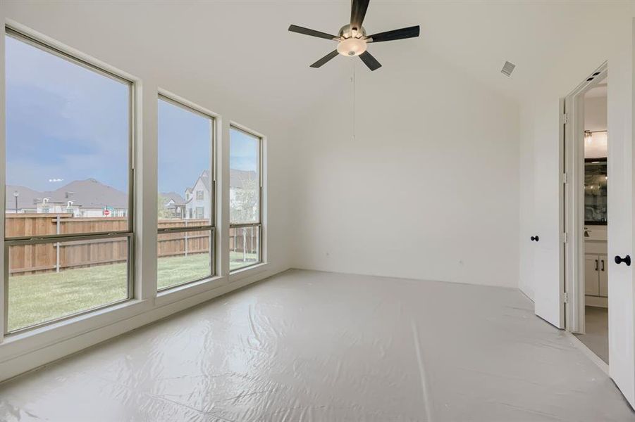 Bright interior space featuring a row of three large windows, a vaulted ceiling with a ceiling fan, and a view of a fenced backyard Bright interior space featuring a row of three large windows, a vaulted ceiling with a ceiling fan, and a view of a fenced backyard