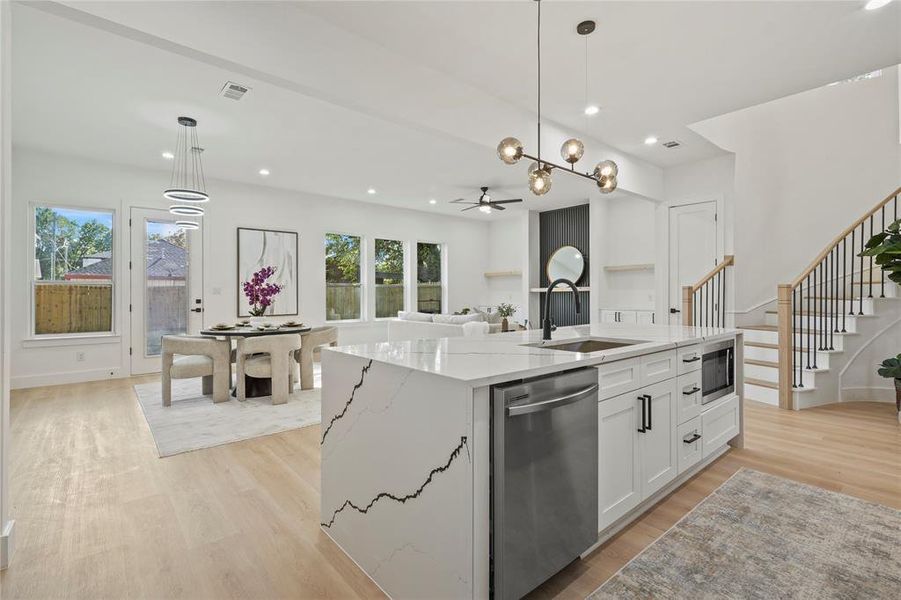 Kitchen featuring a kitchen island with sink, white cabinetry, light stone countertops, stainless steel appliances, and decorative light fixtures
