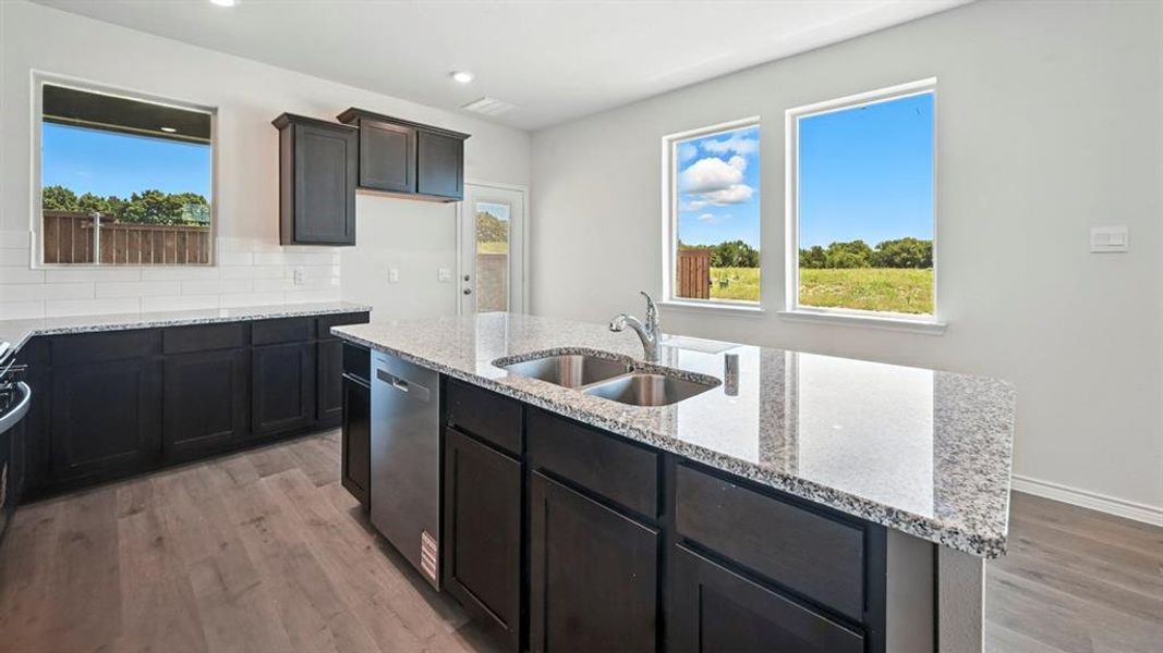 Kitchen with backsplash, light wood-style floors, light stone countertops, dishwasher, and a kitchen island with sink