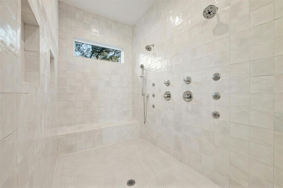 Amazing walk-in shower designed for two with separate shower heads, 6 wall jets, a wall wand, bench seating, designer tile surround, and a clerestory window.