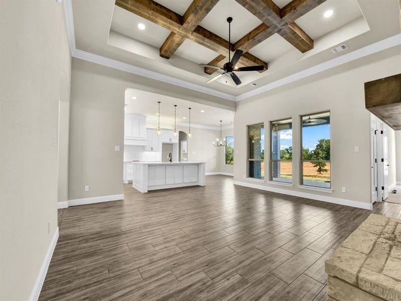 Unfurnished living room featuring beamed ceiling, ceiling fan with notable chandelier, crown molding, and coffered ceiling