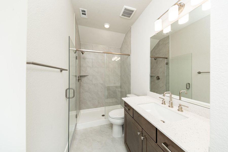 Secondary bath features tile flooring, walk-in shower with tile surround, stained cabinets, beautiful light countertops, mirror, sleek brushed nickel fixtures and modern finishes!
