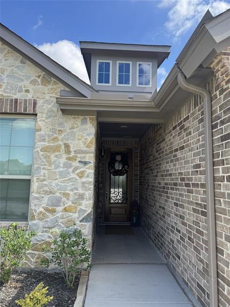 Inviting entry featuring a paneled wood door with decorative ironwork, brick and stone exterior accents, and a dormer with three windows