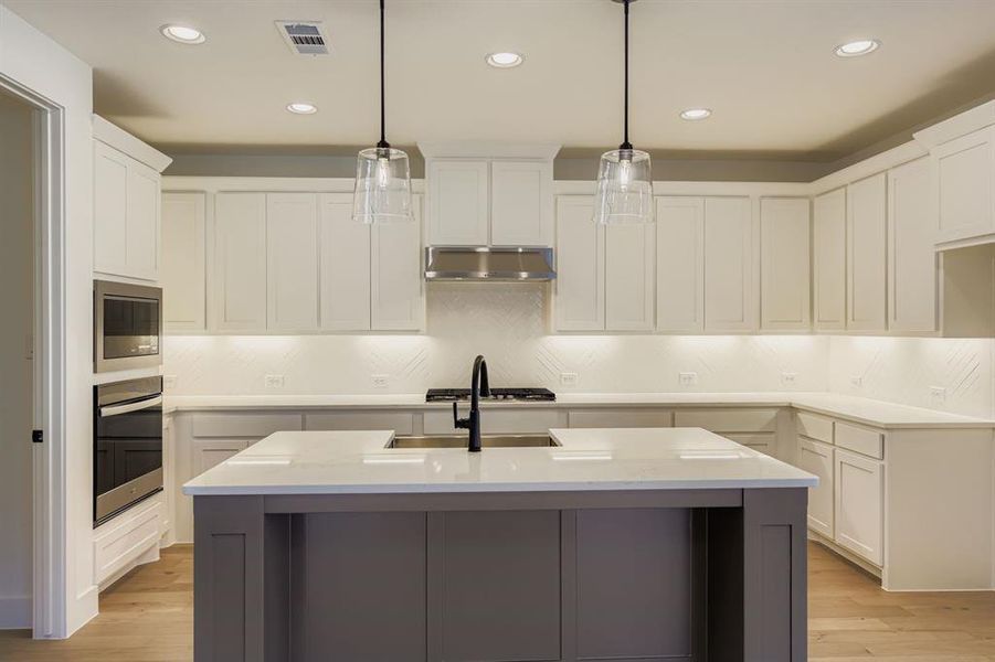 Kitchen with white cabinets, a kitchen island with sink, light wood finished floors, decorative backsplash, and recessed lighting Kitchen with white cabinets, a kitchen island with sink, light wood finished floors, decorative backsplash, and recessed lighting