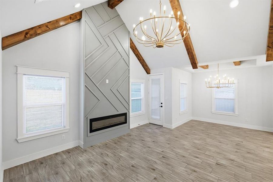 Unfurnished living room with a chandelier, beamed ceiling, a fireplace, light wood-style floors, and high vaulted ceiling