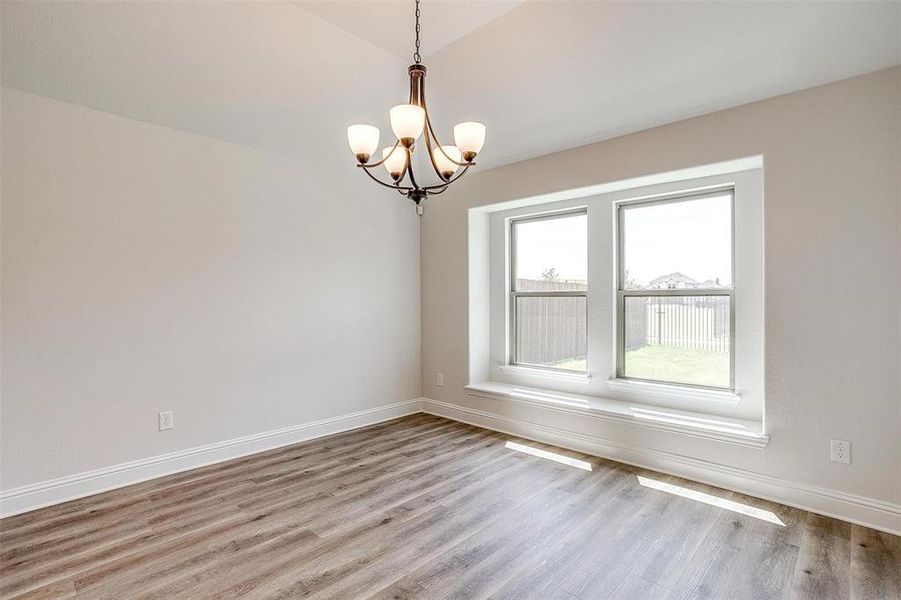 Unfurnished room featuring lofted ceiling, wood-type flooring, and an inviting chandelier