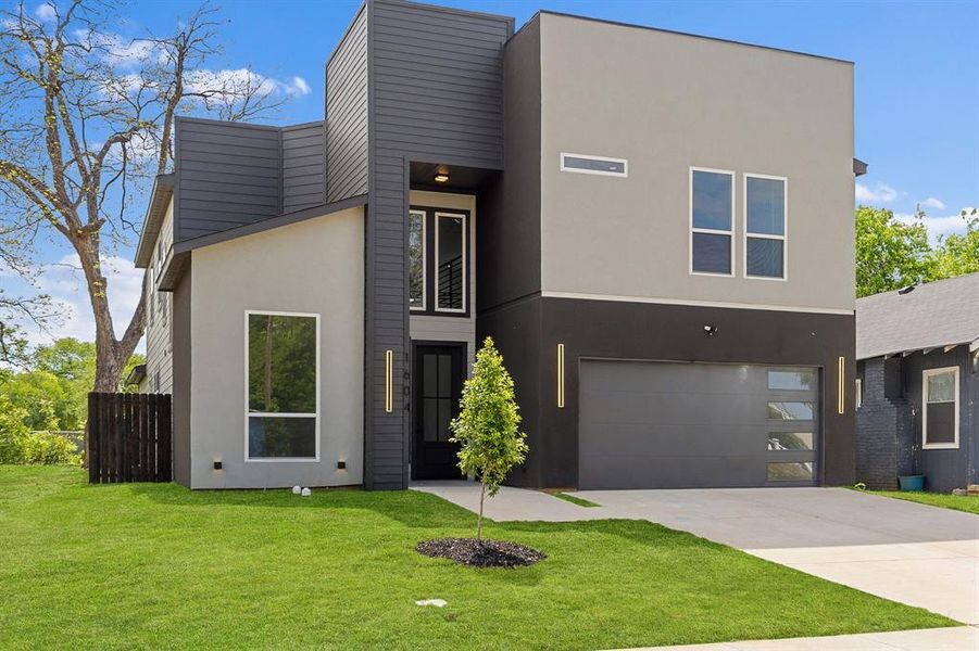 The property features a contemporary architectural style with a two-tone facade, a modern garage door with frosted glass panels, and a well-maintained lawn The property features a contemporary architectural style with a two-tone facade, a modern garage door with frosted glass panels, and a well-maintained lawn
