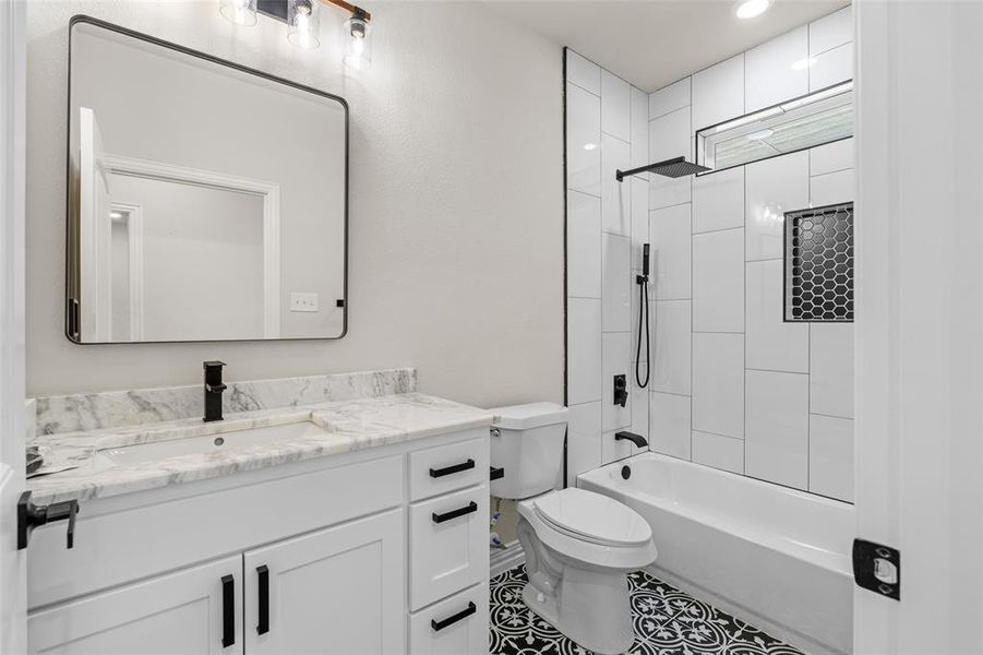 Full bathroom featuring vanity, tiled shower / bath combo, toilet, and tile patterned flooring