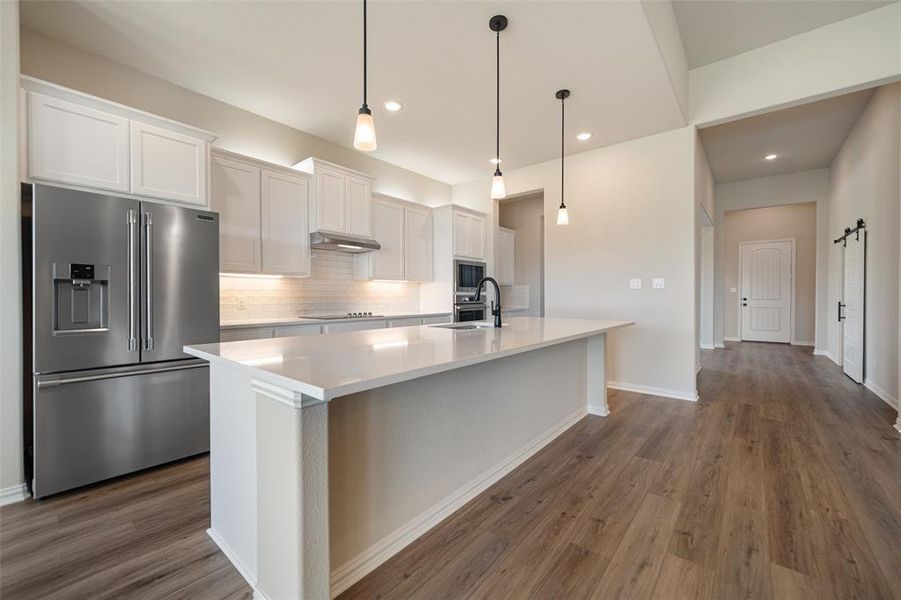 Kitchen with appliances with stainless steel finishes, white cabinetry, tasteful backsplash, decorative light fixtures, and dark wood-type flooring