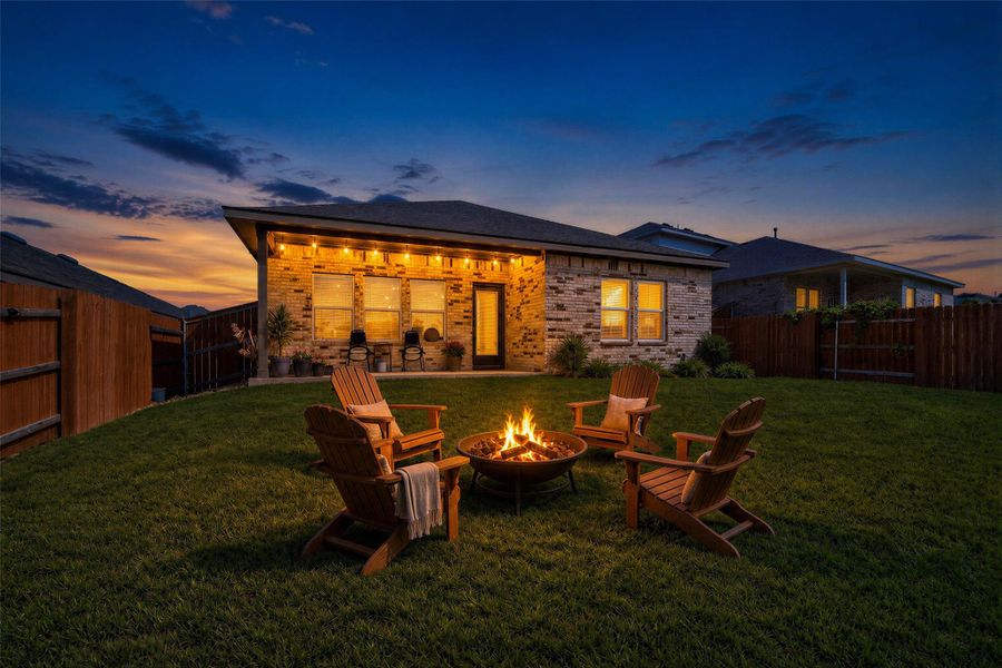 Virtually staged - View of backyard featuring a verdant lawn provides a serene setting for a backyard fire pit, framed by a welcoming patio and brick home.