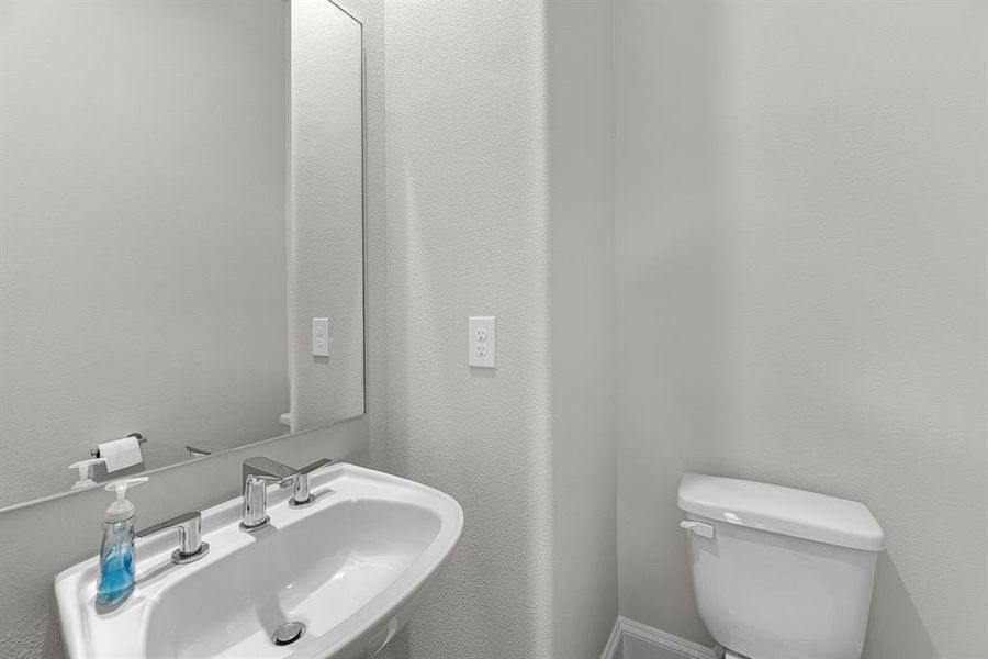 Situated on the second floor, a convenient half bathroom features a stylish pedestal sink and a frameless mirror, providing a chic and functional space for both guests and residents.