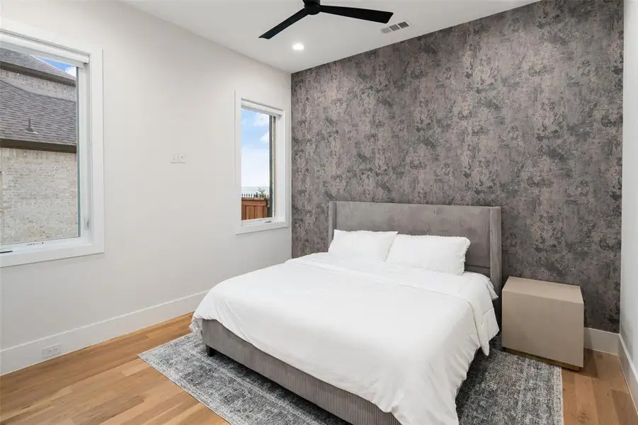 First-floor guest bedroom featuring beautiful lake views, a stylish accent wall, and real hardwood floors. The private ensuite bathroom includes a walk-in shower, offering comfort and convenience for guests or multigenerational living.