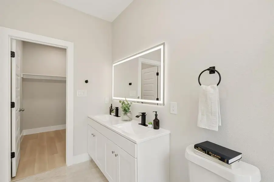 White double vanity with integrated sinks and matte black fixtures, illuminated by a backlit mirror White double vanity with integrated sinks and matte black fixtures, illuminated by a backlit mirror