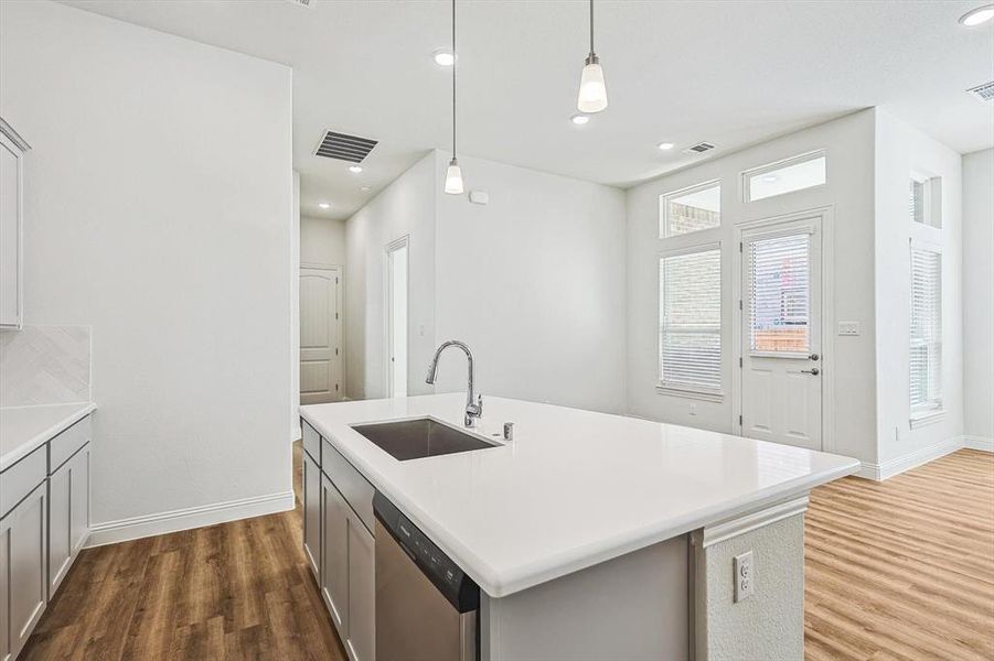 Kitchen with pendant lighting, dishwasher, sink, an island with sink, and hardwood / wood-style floors