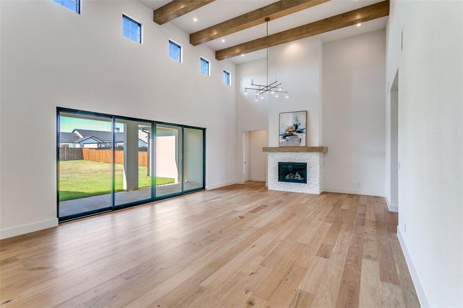 Unfurnished living room featuring beam ceiling, a chandelier, light wood-style floors, a glass covered fireplace, and a high ceiling