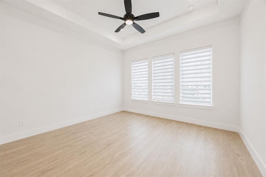 Spacious room featuring wood-finish flooring, a tray ceiling, and a black ceiling fan with integrated lighting