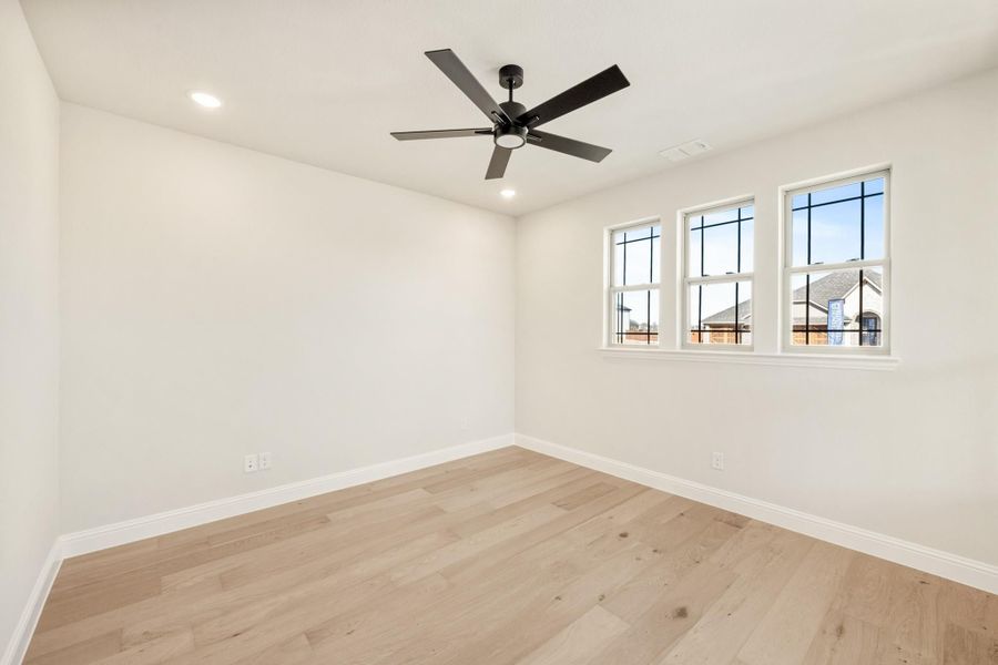 Empty bedroom with light hardwood floors, black ceiling fan, and three windows