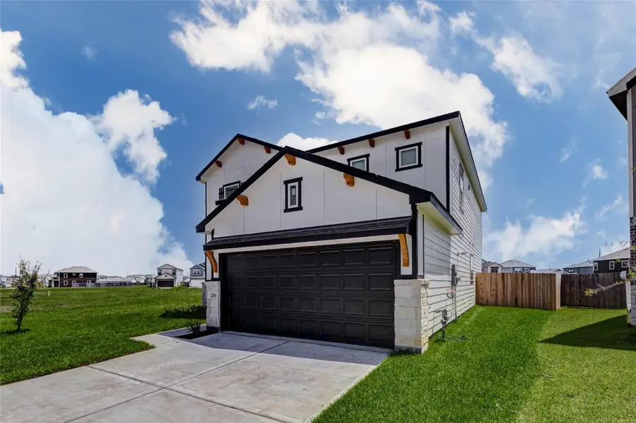 Striking front exterior showcasing a fresh new construction design with crisp white siding, bold black trim, warm wood accent brackets, stone column details, and a dark two-car garage door. The wide driveway, manicured green lawn, and open side yard create an inviting first impression, while the bright blue sky highlights the home’s clean architectural lines and modern traditional curb appeal. Striking front exterior showcasing a fresh new construction design with crisp white siding, bold black trim, warm wood accent brackets, stone column details, and a dark two-car garage door. The wide driveway, manicured green lawn, and open side yard create an inviting first impression, while the bright blue sky highlights the home’s clean architectural lines and modern traditional curb appeal.