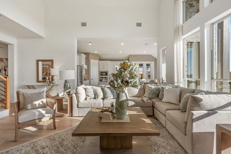 Open-concept living room with high ceilings, sectional sofa, wood coffee table, and kitchen visible in background
