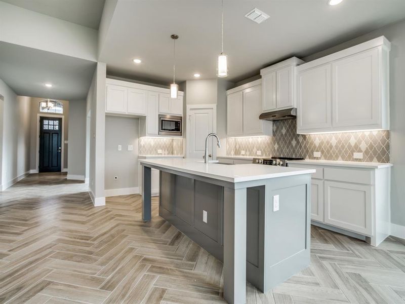 Kitchen with decorative backsplash, stainless steel microwave, under cabinet range hood, and a sink