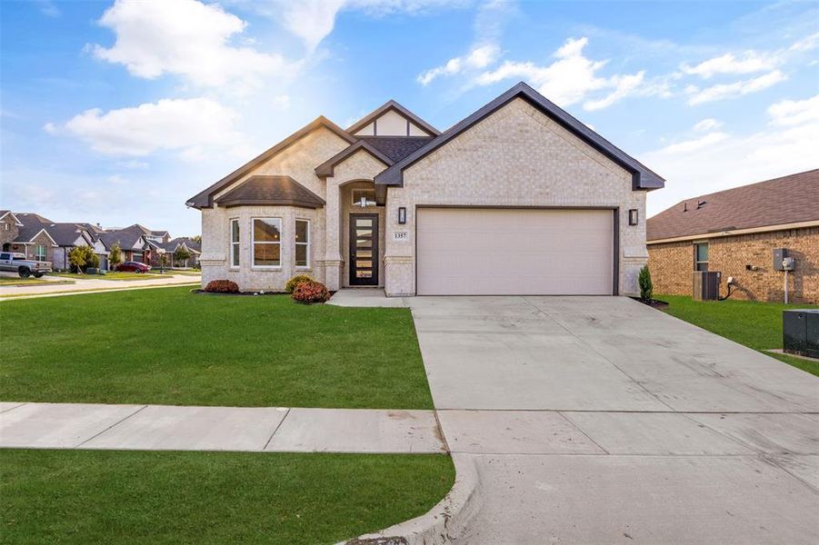 View of front of property with brick siding, driveway, a front yard, and a garage