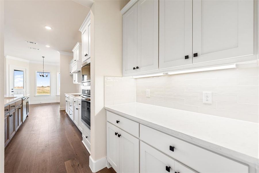 Kitchen with white cabinets, ornamental molding, dark wood-type flooring, recessed lighting, and light stone countertops