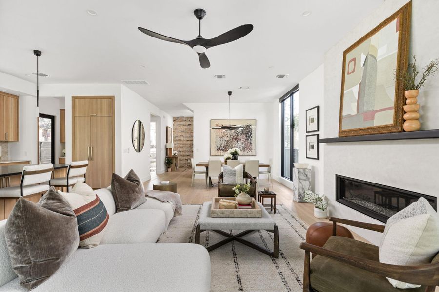 Living room with a glass covered fireplace, light wood-style flooring, ceiling fan, and a chandelier Living room with a glass covered fireplace, light wood-style flooring, ceiling fan, and a chandelier