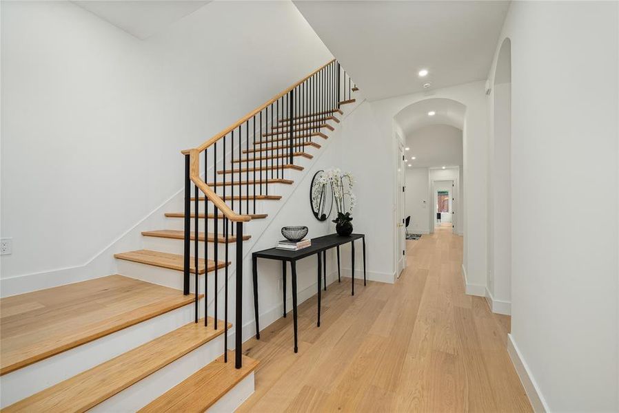 Entryway featuring a wooden staircase with black iron railings, light hardwood flooring, and an arched hallway
