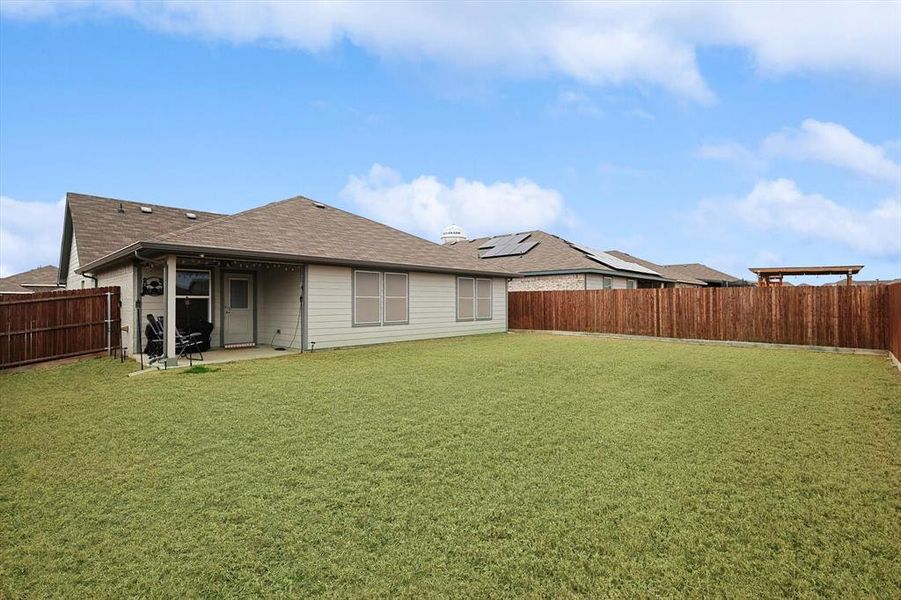 Rear view of property featuring a patio area, a fenced backyard, a lawn, and roof with shingles