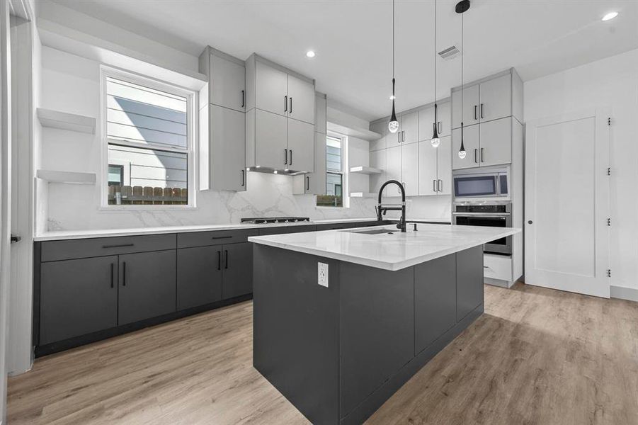 Kitchen with pendant lighting, sink, a center island with sink, light hardwood / wood-style floors, and appliances with stainless steel finishes