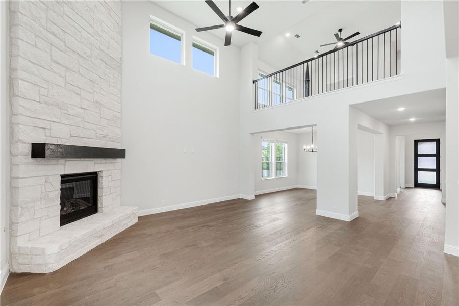 Open living room with two-story ceiling, stone fireplace, hardwood floors, and second-floor balcony overlook Open living room with two-story ceiling, stone fireplace, hardwood floors, and second-floor balcony overlook