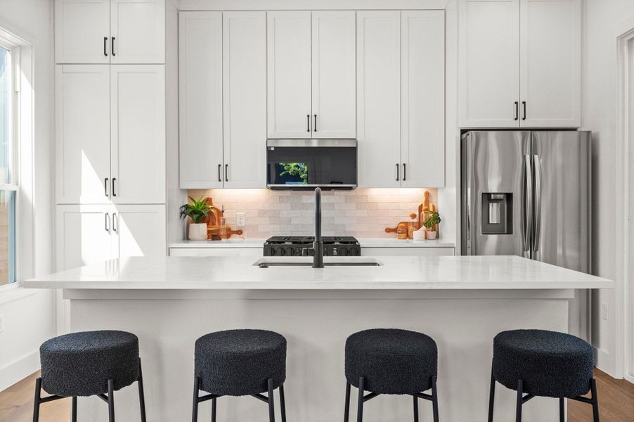 Kitchen with light wood finished floors, a breakfast bar area, decorative backsplash, light stone countertops, and white cabinets