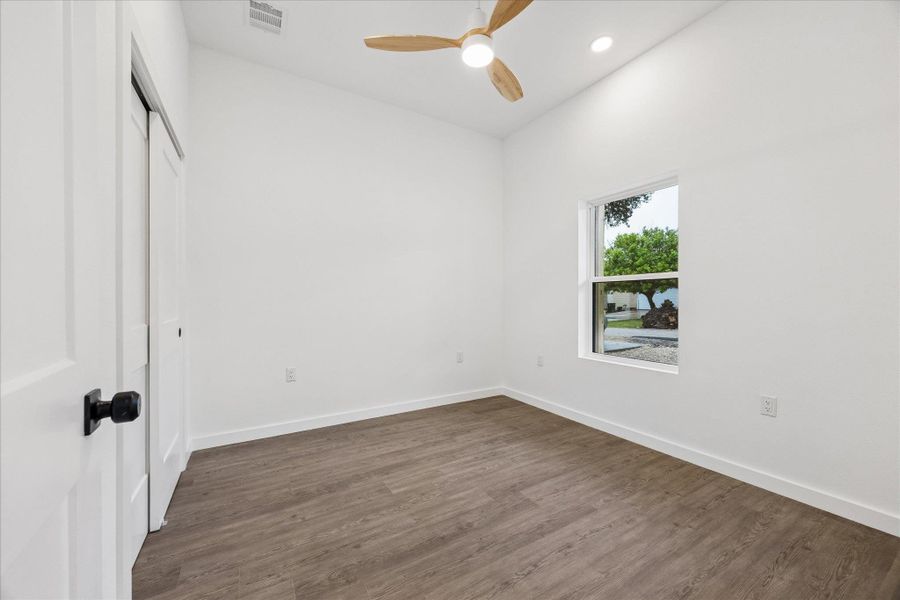 A quiet bedroom showcases contemporary flooring, a ceiling fan, and a view of the peaceful outdoors.