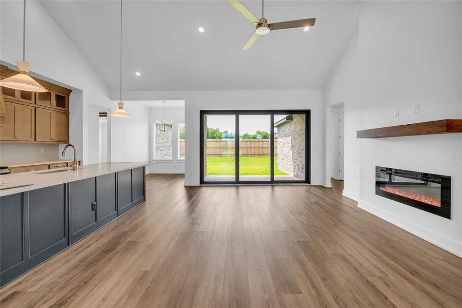 Unfurnished living room with a glass covered fireplace, ceiling fan, high vaulted ceiling, light wood-type flooring, and a sink