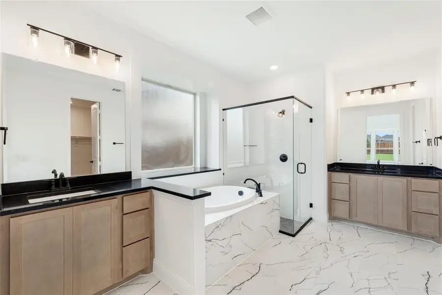 Master bathroom with dual vanities, soaking tub, glass shower, and marble tile floors