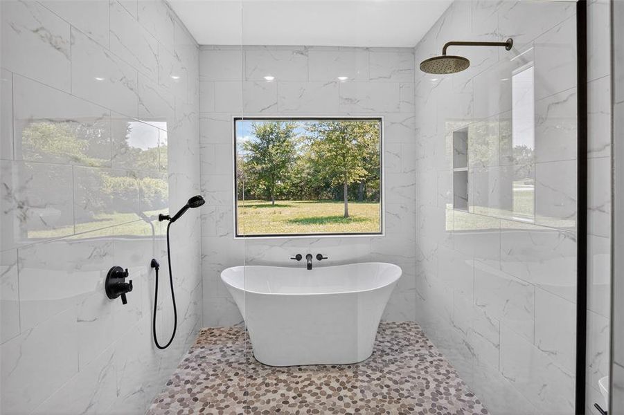 Primary Modern bathroom featuring a standalone soaking tub with wall-mounted faucet, matte black fixtures, pebble-tile flooring, and large format white tile walls Primary Modern bathroom featuring a standalone soaking tub with wall-mounted faucet, matte black fixtures, pebble-tile flooring, and large format white tile walls