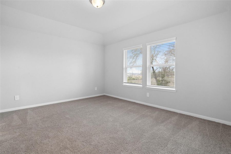 Upstairs, the primary bedroom provides a peaceful escape with a bright, neutral palette, sloped ceilings, large windows, and plush carpet flooring, creating a calm and restorative atmosphere to end your day.