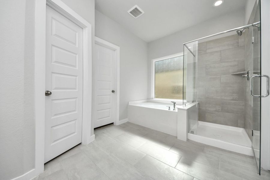 Escape to a spa-like oasis in this primary bathroom. Enjoy a walk-in shower with tile surround, a separate garden tub with custom detailing, and an elegant vanity featuring light countertops, modern hardware, and beautiful vanity lights. Experience luxury and relaxation in every detail. Sample photo of completed home with similar floor plan. Actual colors and selections may vary.