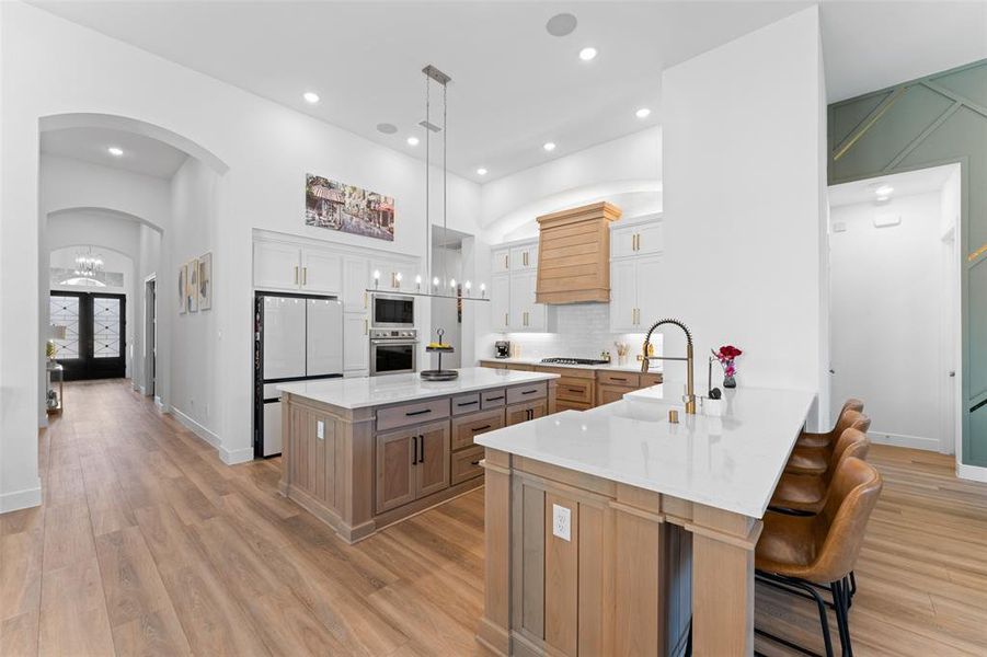 The expansive kitchen features light wood flooring, white cabinetry, and a large kitchen island with a white countertop