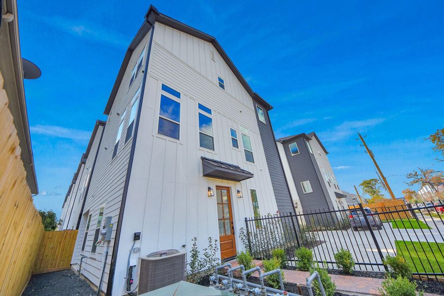 Notice the mix of white and dark siding on this three-story home, with a gated front yard and garden framing the entrance. Light pours through abundant windows, illuminating the interior.