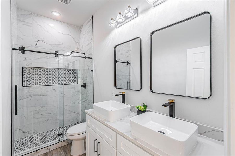 Bathroom with a marble finish shower, double vanity, and wood finished floors