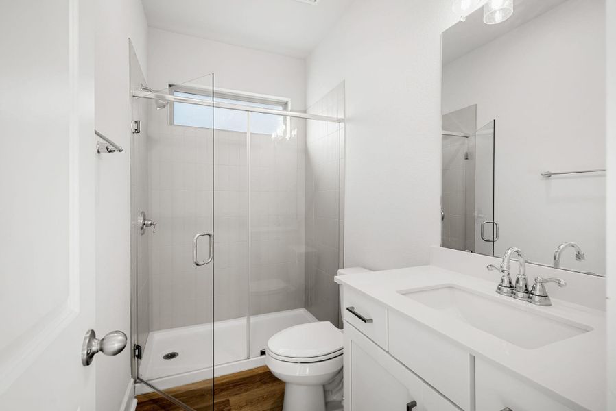 A sleek vanity with ample storage complements the clear glass shower enclosure, creating a fresh, functional bathing space.