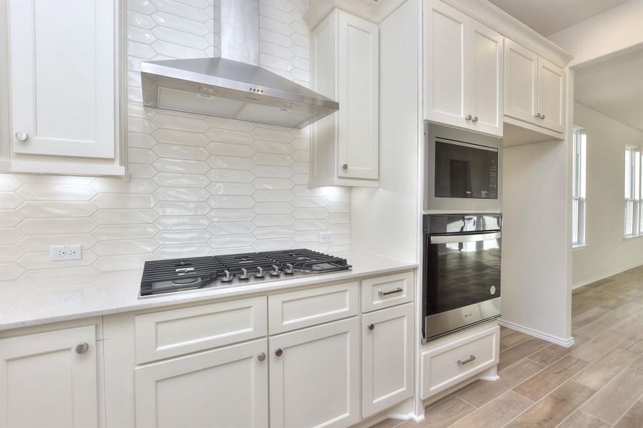 Kitchen featuring stainless steel gas cooktop, decorative backsplash, white cabinetry, wall chimney exhaust hood, and light wood-type flooring