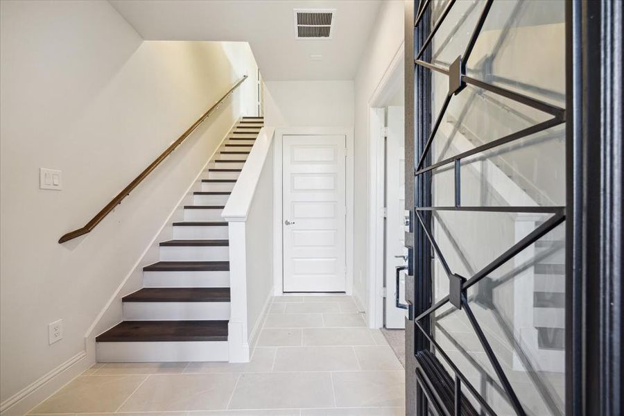 This stylish entryway sets the tone for this 3-bedroom, 3.5-bathroom home. Sleek tile floors and an open staircase lead up to the main living areas, while a custom-designed front door adds a touch of sophistication. To the right of the entry is a first floor bedroom with ensuite bathroom.