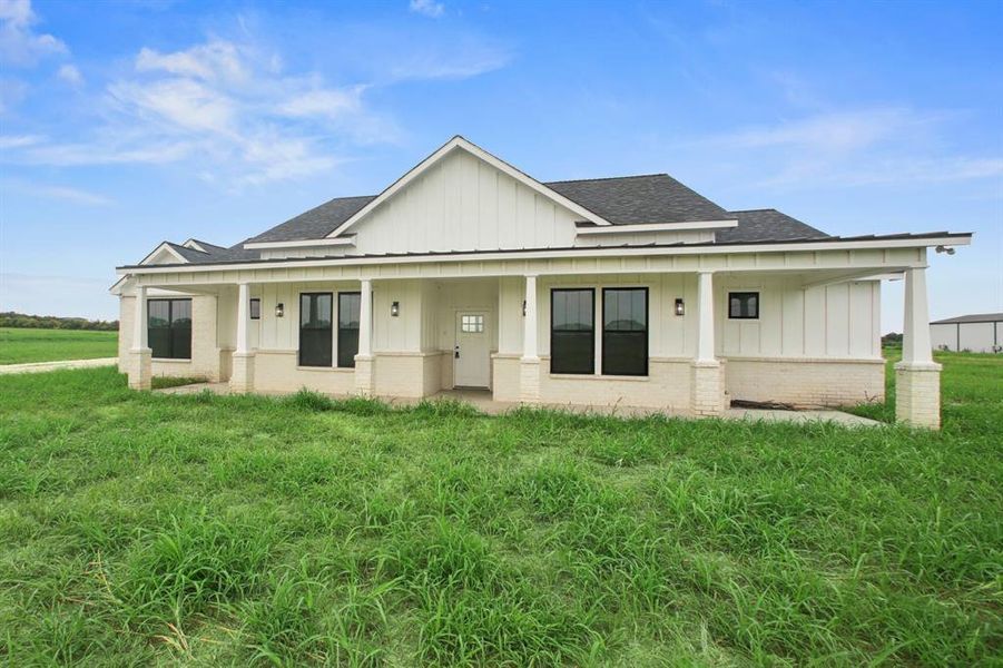 View of front facade with board and batten siding, roof with shingles, covered porch, and a front lawn
