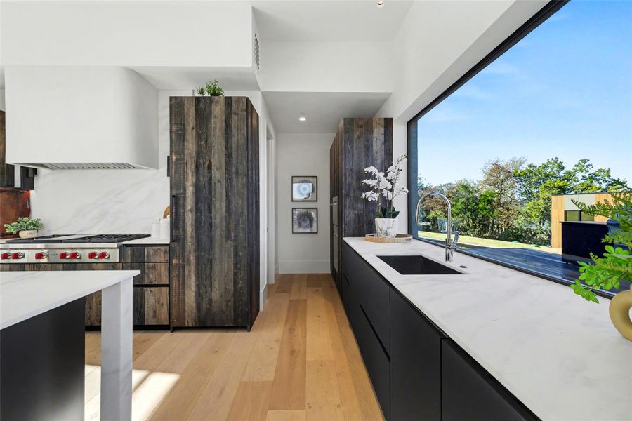 Kitchen featuring light stone counters, light wood-style flooring, modern cabinets, wall chimney range hood, and dark cabinets