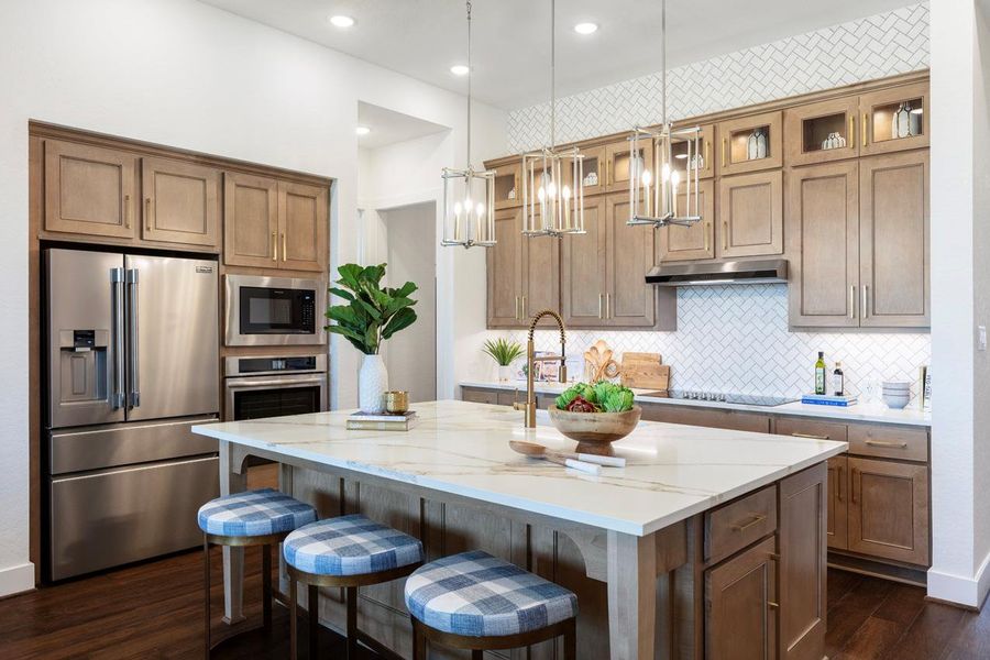 Kitchen with a kitchen island with sink, light stone countertops, stainless steel appliances, under cabinet range hood, and dark wood-style floors Kitchen with a kitchen island with sink, light stone countertops, stainless steel appliances, under cabinet range hood, and dark wood-style floors